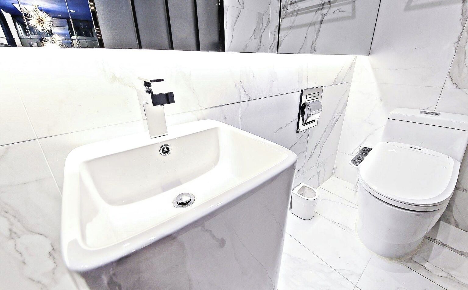 Un baño moderno con un lavamanos blanco, un inodoro y un cubo de basura.