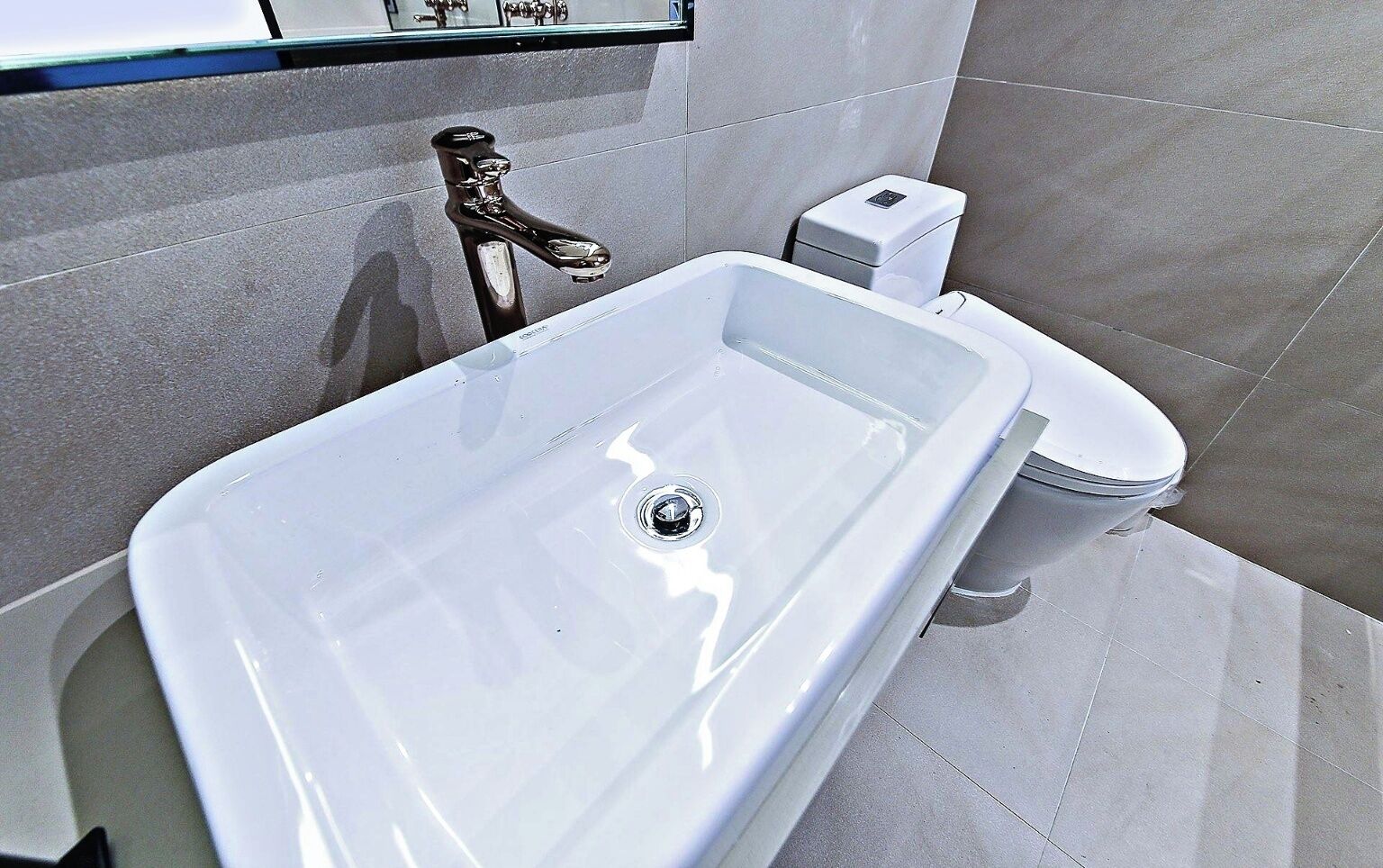 Ein modernes Badezimmer mit einem weißen Waschbecken, einem chromfarbenen Wasserhahn und einer Toilette.