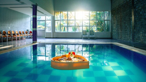 Une piscine avec, en arrière-plan, une pièce baignée de lumière, un espace détente avec des chaises, et une table de buffet garnie de nourriture et de boissons.