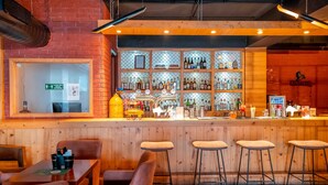 Un espace bar avec des tabourets en bois, un comptoir avec des bouteilles et un panneau indiquant les mesures de distanciation sociale.