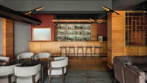 Un espace bar avec des murs en bois, un comptoir et des tabourets. On aperçoit des tables et des chaises au premier plan.