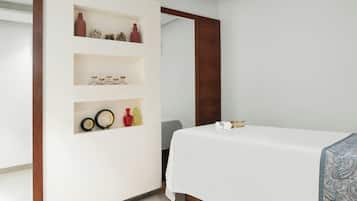 A hotel room with a bed, a white wall with shelves containing decorative items, and a wooden door frame.