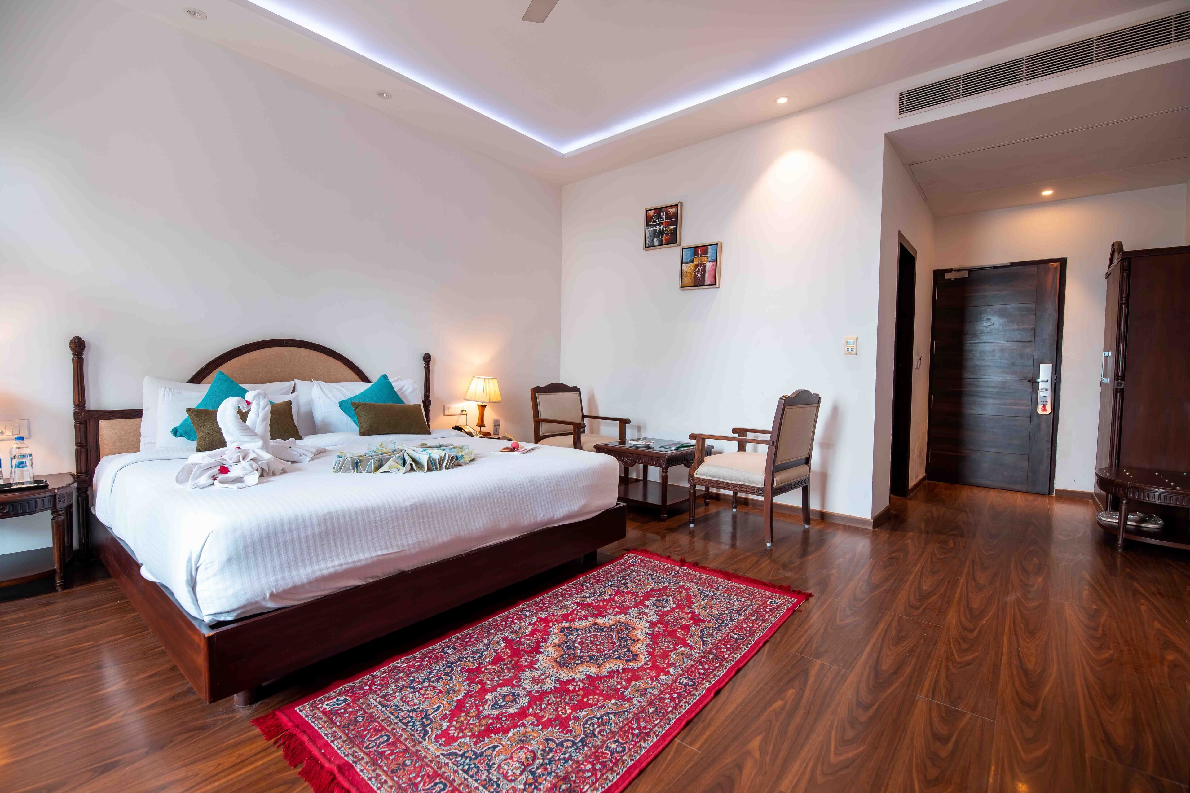 A hotel room with a large bed, a desk, a chair, and a red patterned rug.