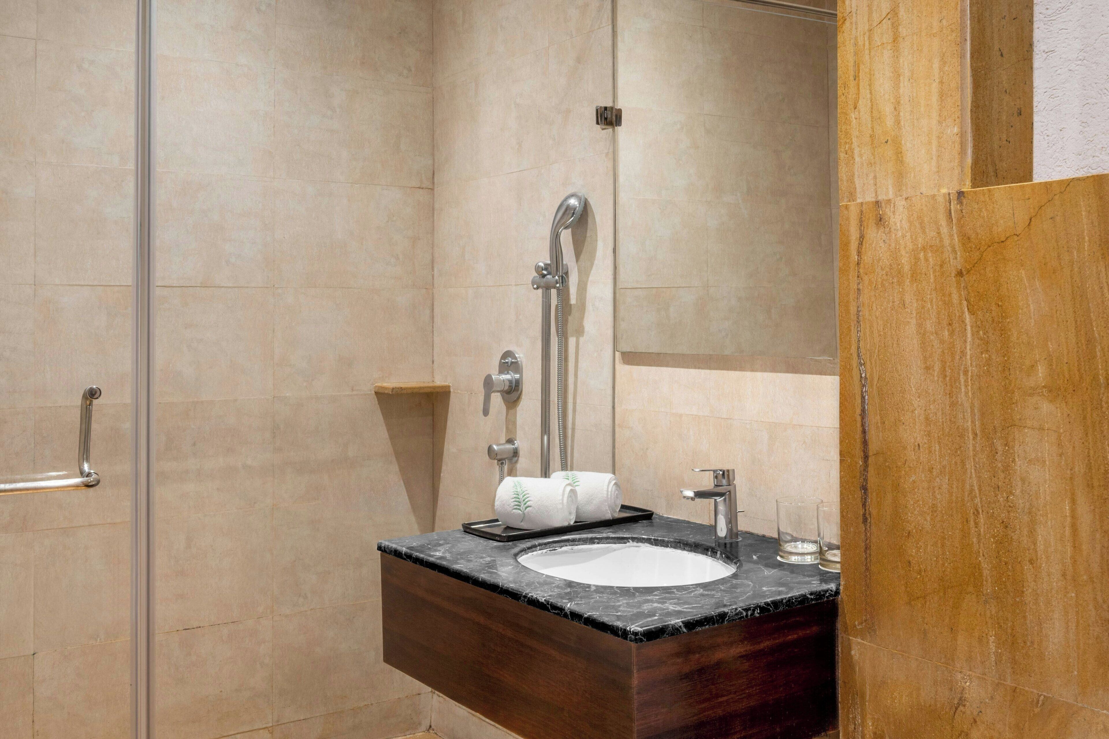 A bathroom with a marble sink, a handheld showerhead, and a towel rack.