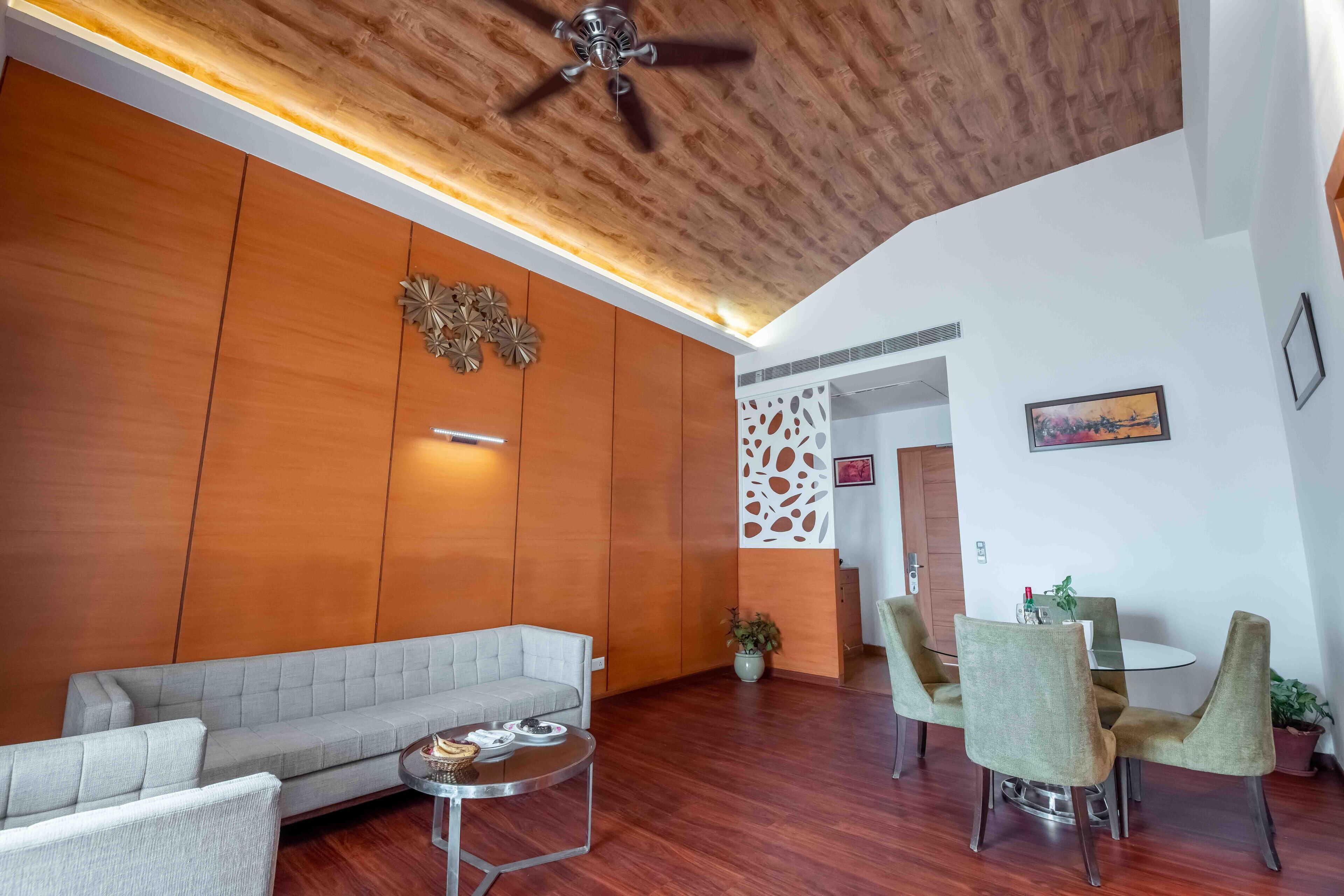 A modern living room with a wooden ceiling, a sofa, a coffee table, and a dining area with chairs and a table.