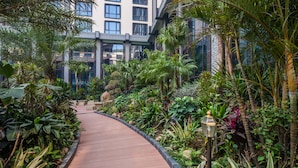 A pathway through a lush garden with a modern building in the background.