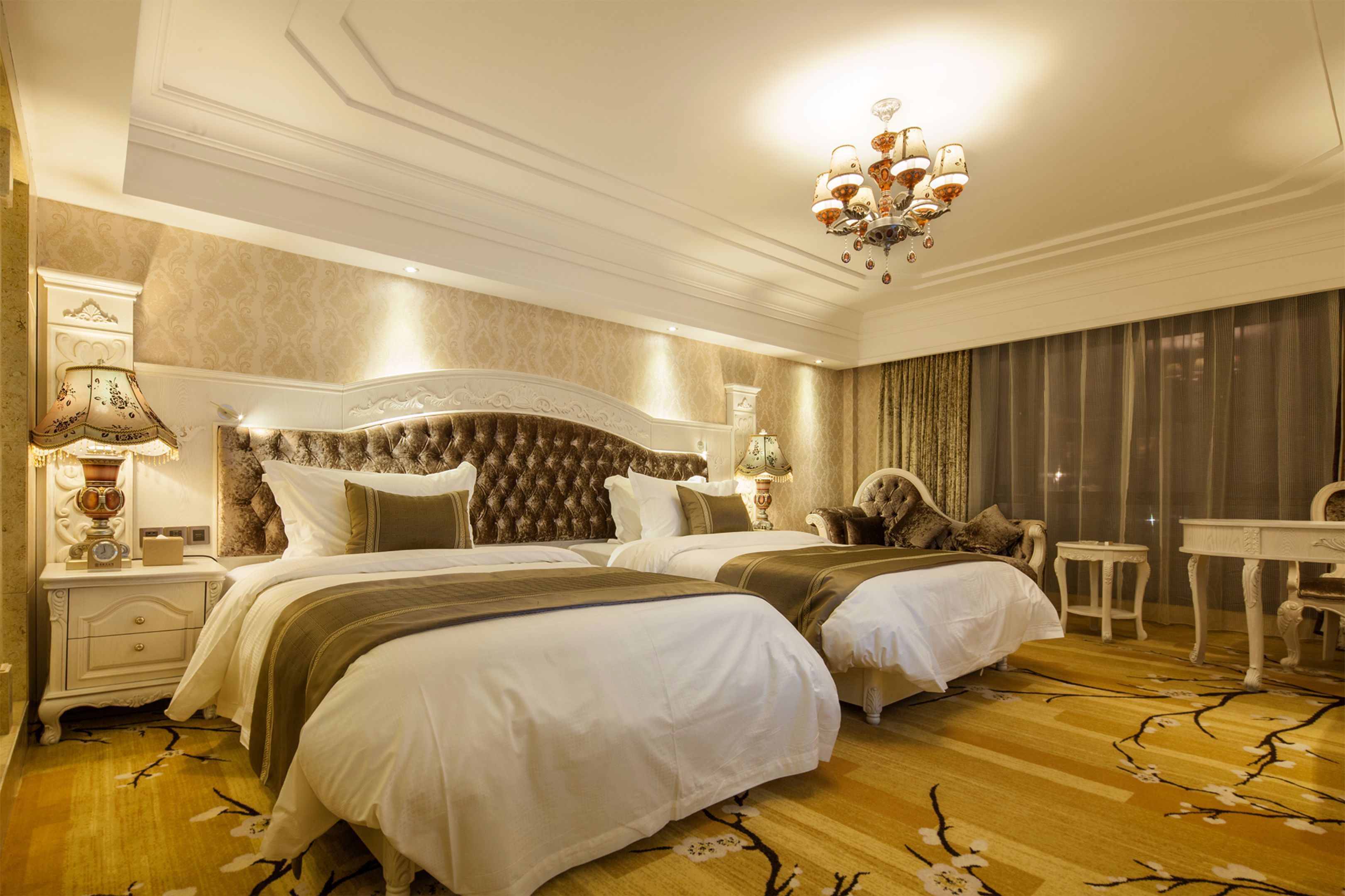 A hotel room with two beds, a chandelier, a desk, and a chair.