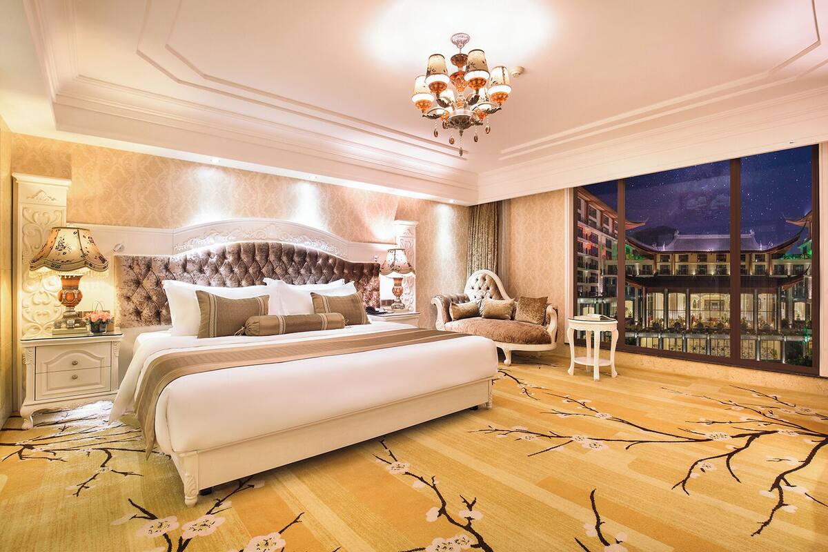 A luxurious bedroom with a large bed, a nightstand, a chair, and a view of a traditional building through a large window.