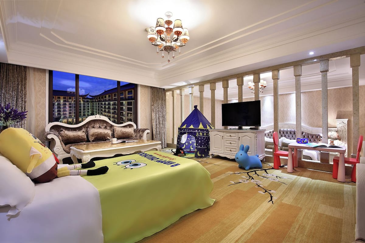 A spacious hotel room with a large bed, a sofa, a television, and a play tent.
