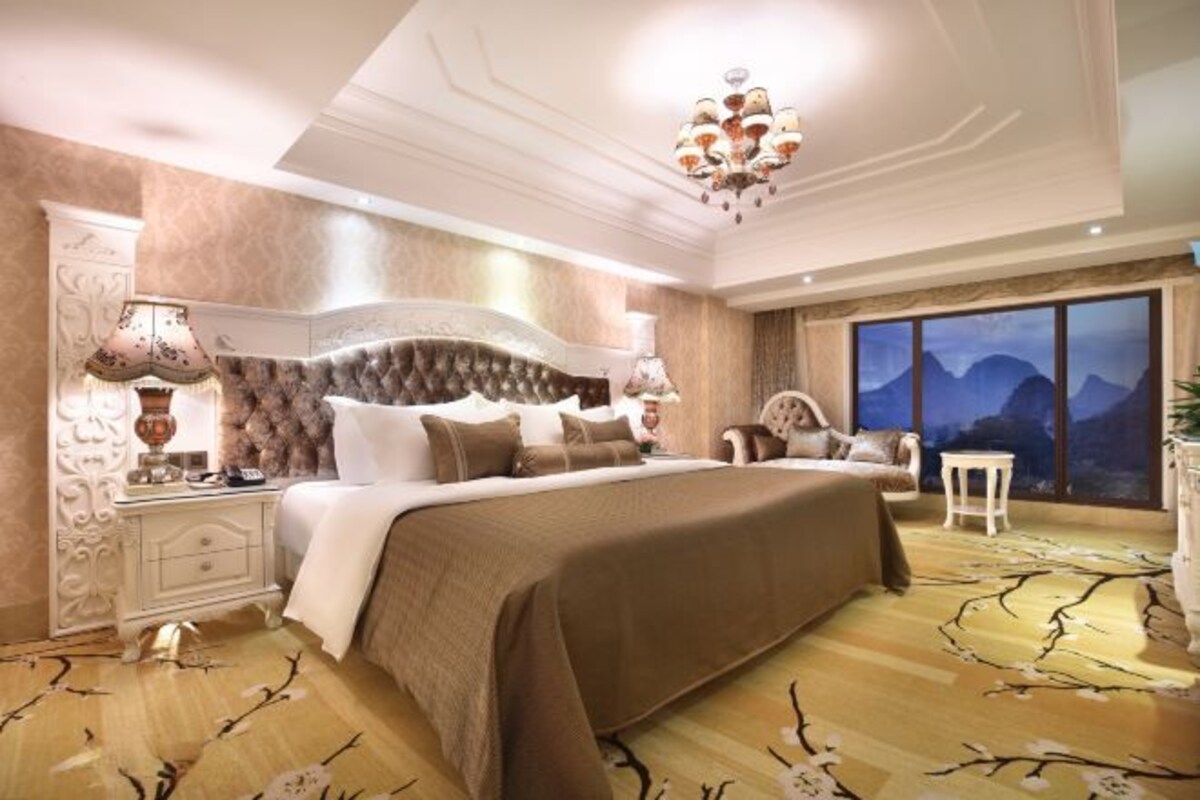 A spacious bedroom with a large bed, a nightstand, a chair, and a view of mountains through the window.