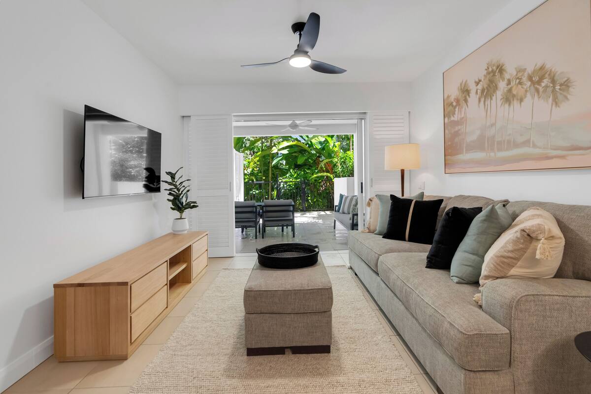 Ein modernes Wohnzimmer mit Sofa, Couchtisch, Fernseher und Deckenventilator.