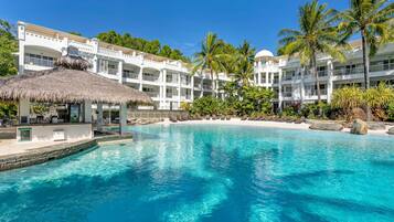 A resort with a large swimming pool, a thatched-roof structure, and multiple white buildings with balconies.