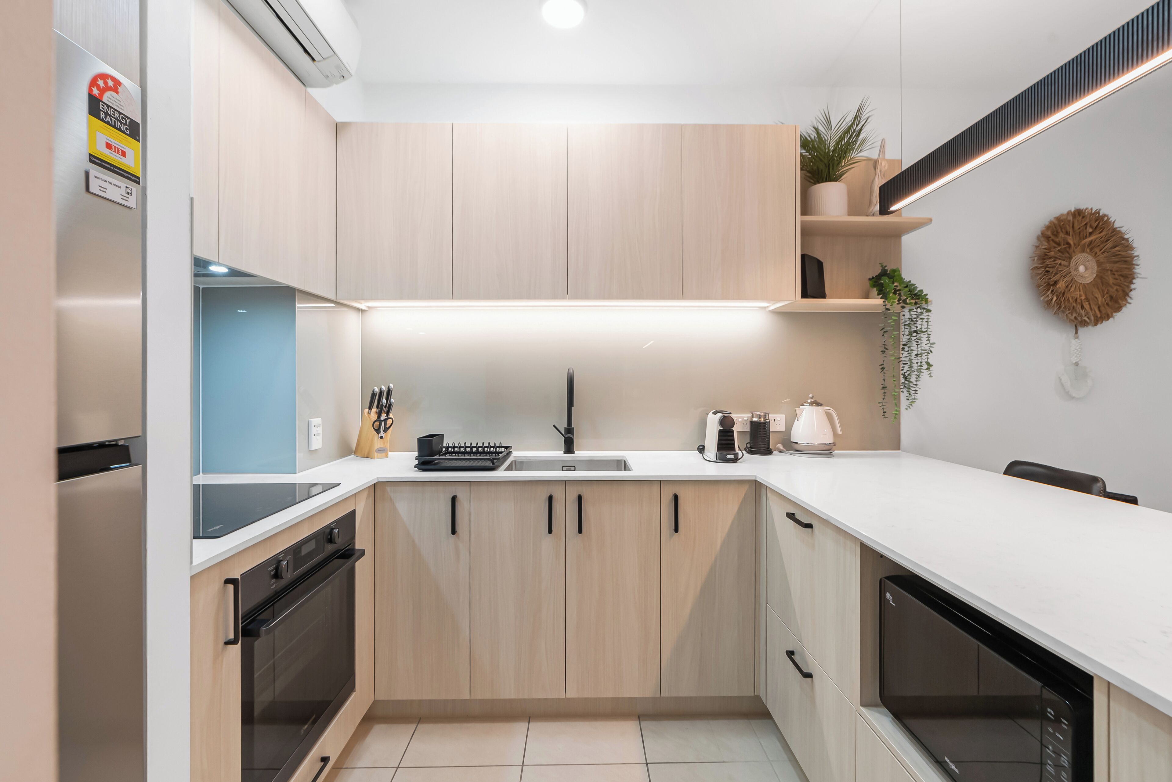 Een moderne keuken met lichte houten kastjes, een ingebouwde oven, een magnetron en een spoelbak.
