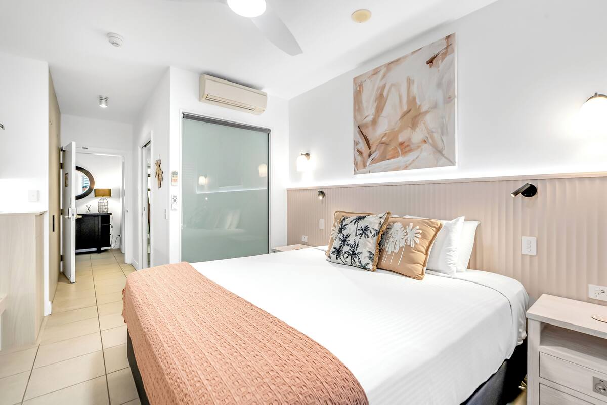 Ein modernes Hotelzimmer mit einem großen Bett, einem Nachttisch, einem Kleiderschrank und einem durch eine offene Tür einsehbaren Badezimmer.