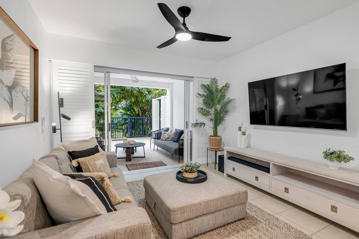 Ein modernes Wohnzimmer mit Sofa, Hocker, Fernseher und Deckenventilator.