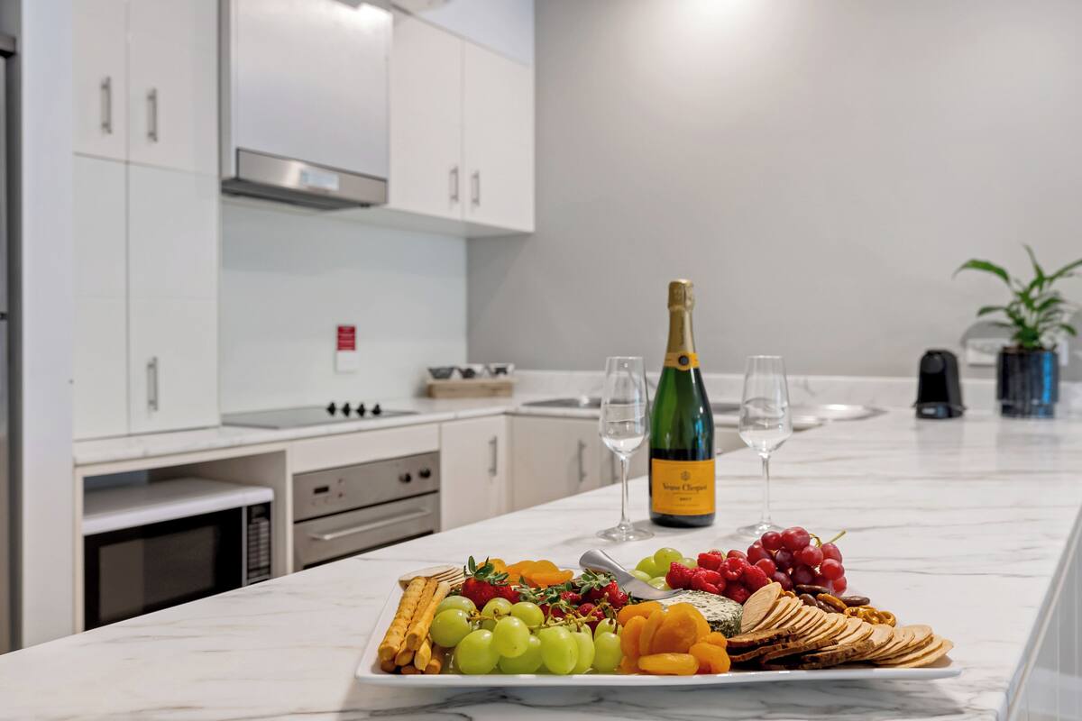 Eine Arbeitsplatte aus Marmor mit einer Obstplatte, Weingläsern und einer Champagnerflasche in einer modernen Küche.