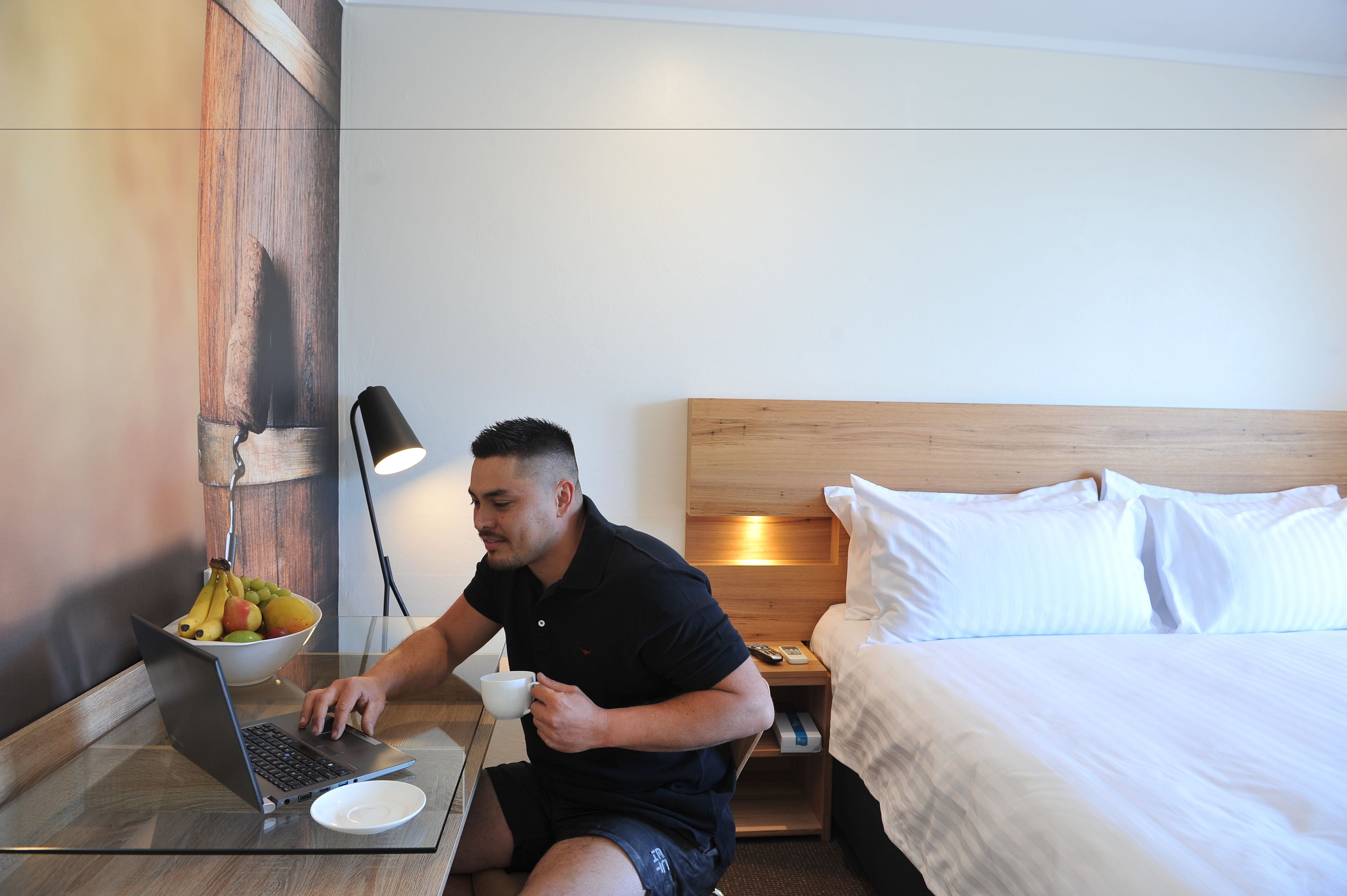 A hotel room with a bed, a bedside table with a lamp, a laptop, and a bowl of fruit.