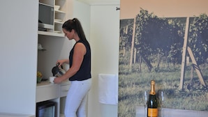 A person pouring a drink into a cup at a kitchen counter with white cabinets and a white towel hanging on the wall. A bottle of champagne and a glass are visible on a table in the foreground.