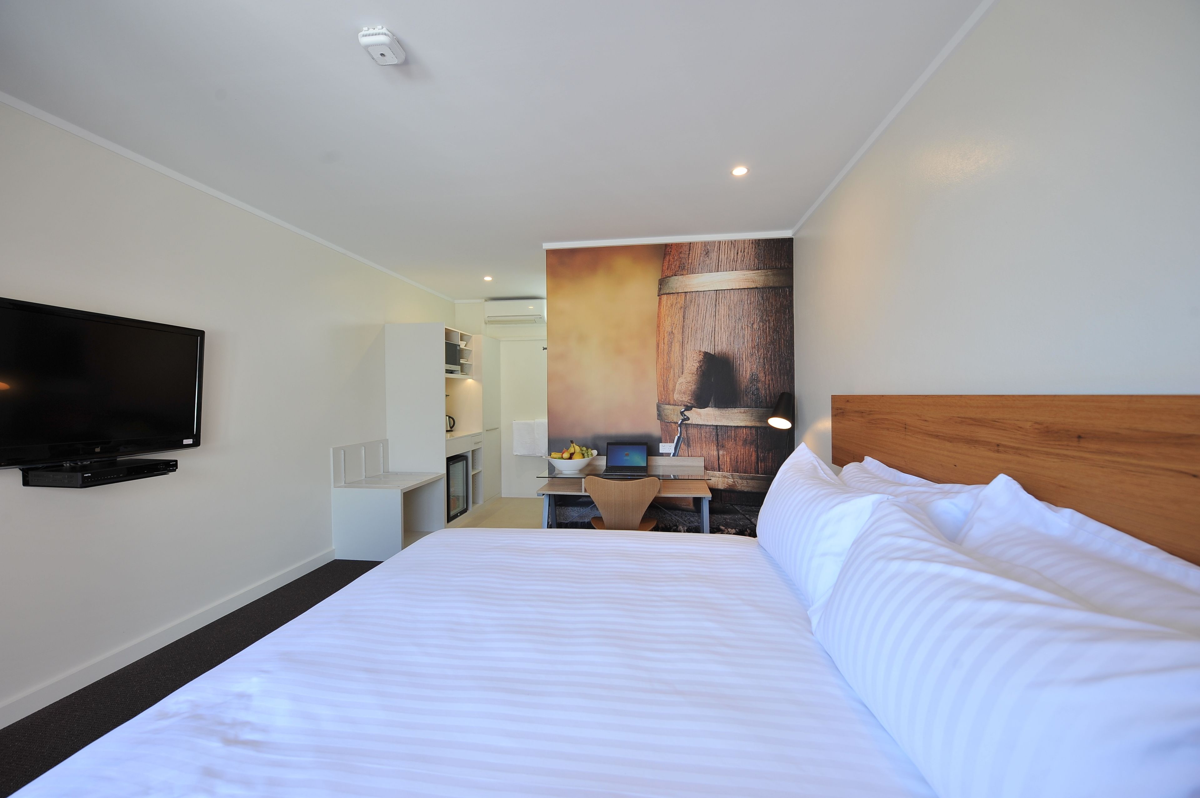Habitación de hotel con una cama grande, un televisor de pantalla plana en la pared, un escritorio con una computadora portátil y un frutero.