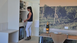 A modern kitchen with white cabinetry, a built-in microwave, and a small refrigerator. There is a glass table with a bottle of champagne and a glass on it.
