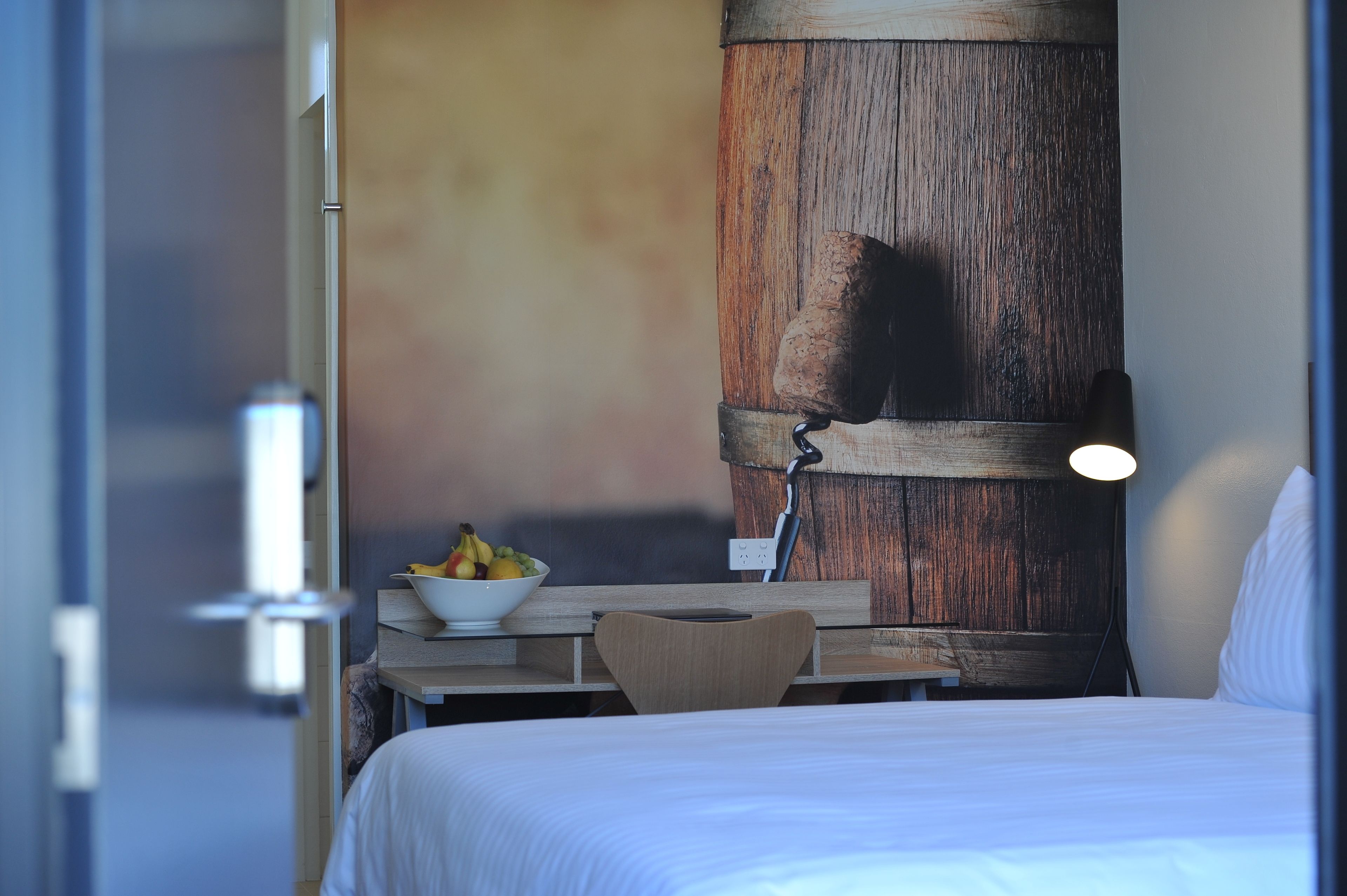 Habitación de hotel con cama, un panel decorativo de madera, una mesa con fruteros y una silla.