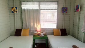 A small, cozy room with two single beds, a small table with a lamp, and a window with lace curtains. - Baanklangsoi (Prachuap Khiri Khan)