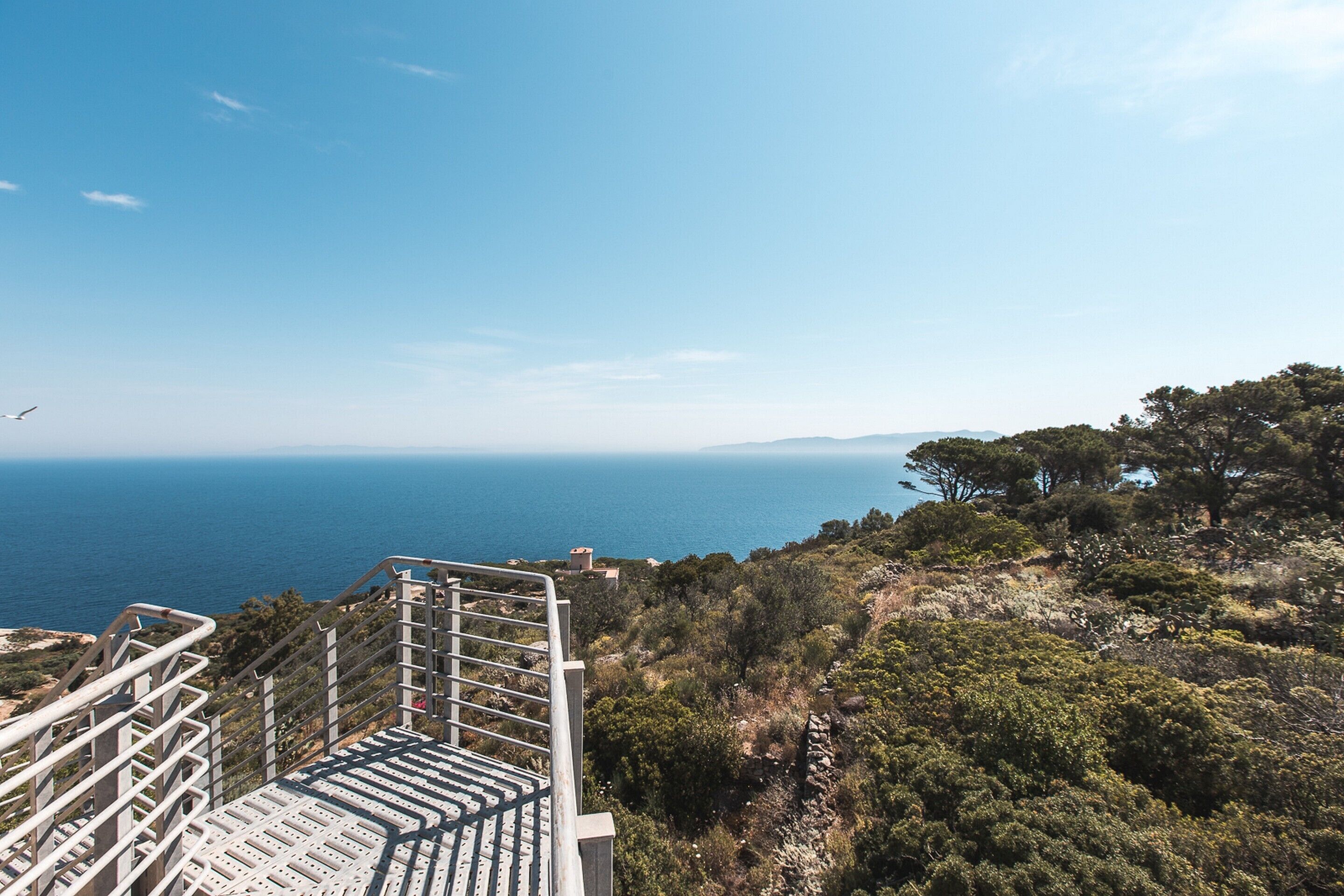 Un escalier menant à un belvédère offrant une vue panoramique sur la mer et les montagnes lointaines.