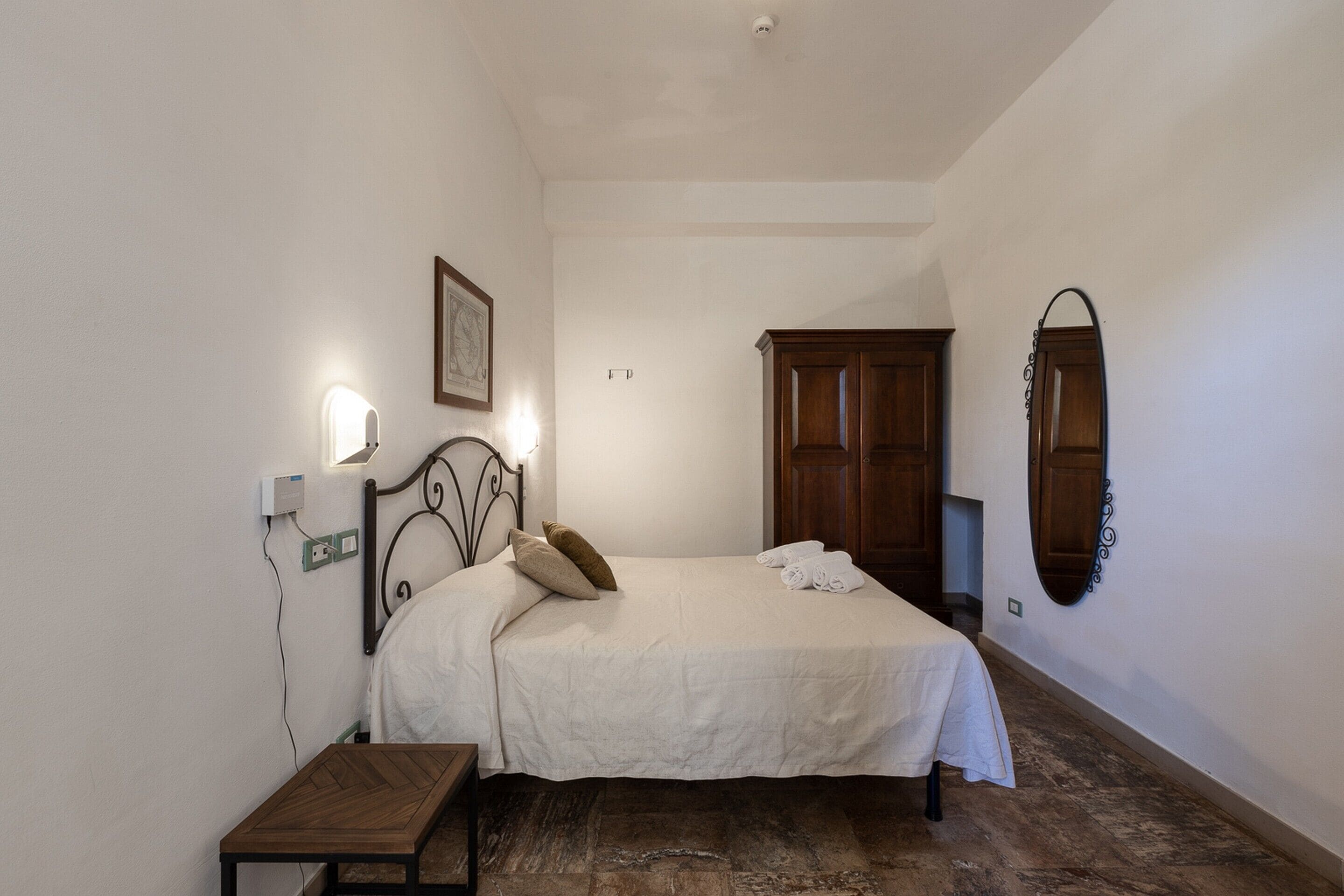 Ein Schlafzimmer mit Bett, Nachttisch, Wandlampe und Spiegel.