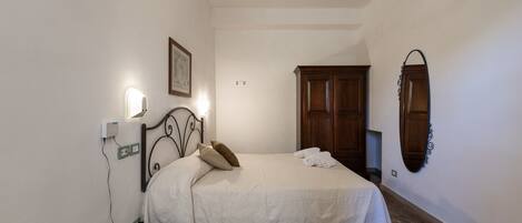 A bedroom with a bed, bedside table, wall-mounted light, and a mirror.