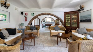 Uma sala de estar espaçosa com móveis de vime, um armário de madeira e uma cozinha ao fundo.