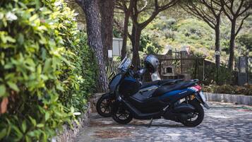 Uma motocicleta estacionada em um caminho de pedras irregulares, com árvores e vegetação ao fundo.