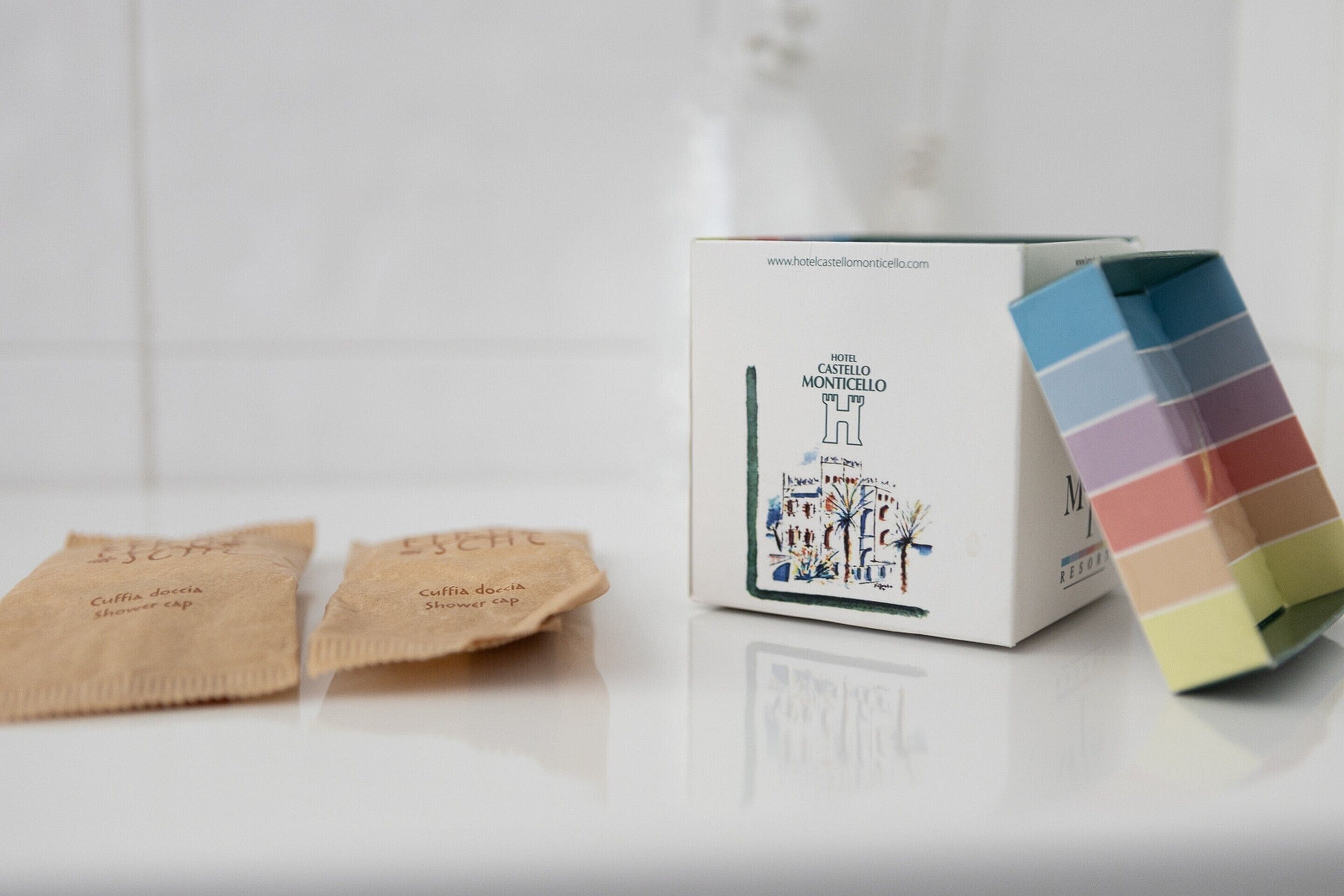 A hotel box with a color palette and two brown paper towels labeled "Cuffia doccia Shower cap".