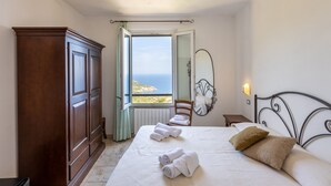 Quarto com cama, guarda-roupa, cadeira, mesa de cabeceira, espelho e vista para o mar.