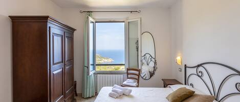 Un dormitorio con cama, armario, silla, mesita de noche, espejo y vista al mar.