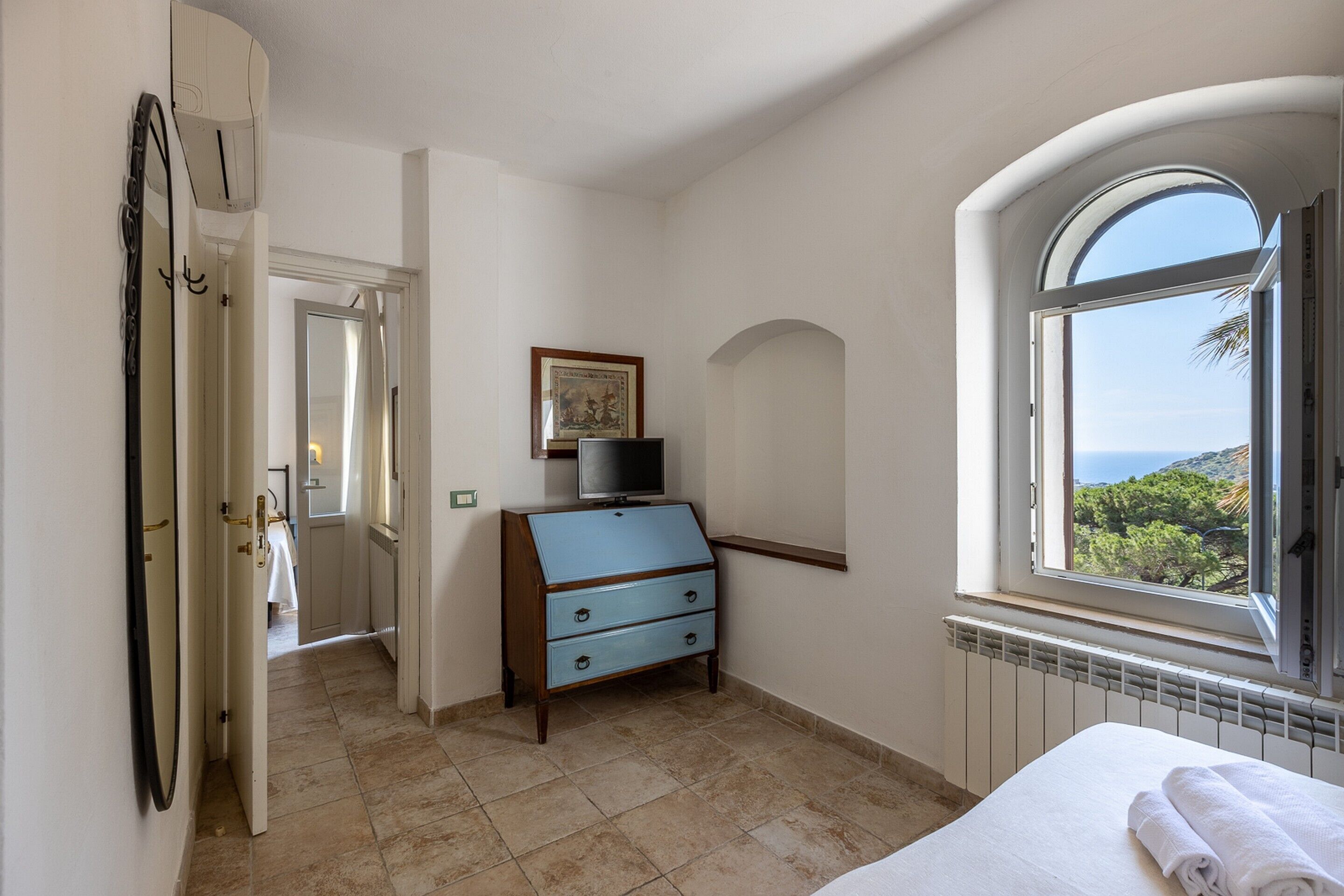 A bedroom with a bed, a dresser, a television, and a window with a view.