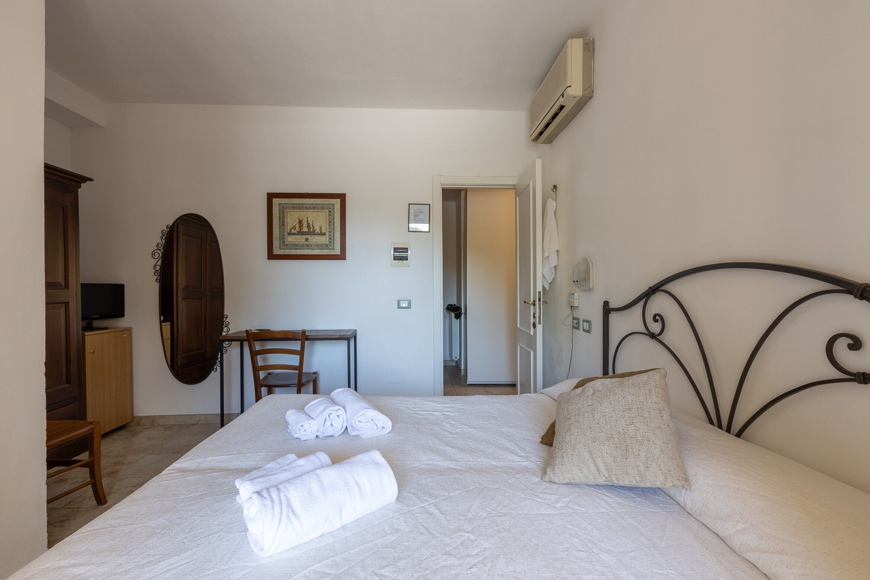 Una habitación de hotel con cama, escritorio, silla, televisor y aire acondicionado.