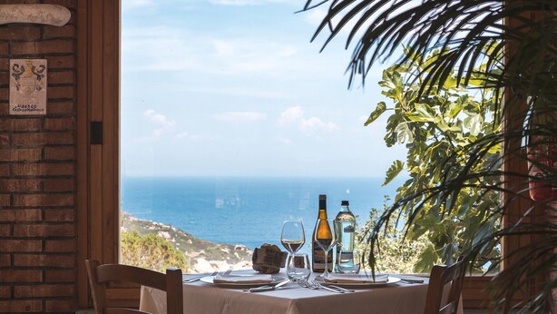 Mesa posta para dois, com vista para o mar, uma garrafa de vinho e um copo de água sobre a mesa.