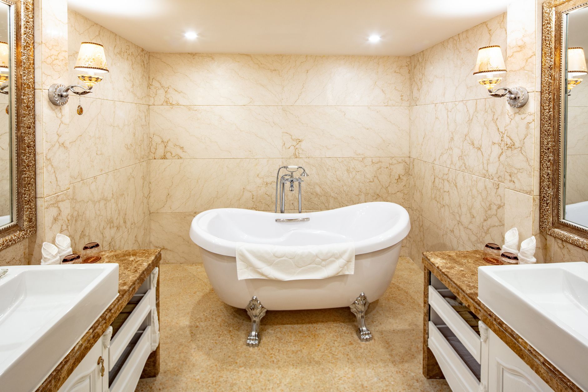 A bathroom with a freestanding bathtub, two sinks, marble walls, and wall sconces.