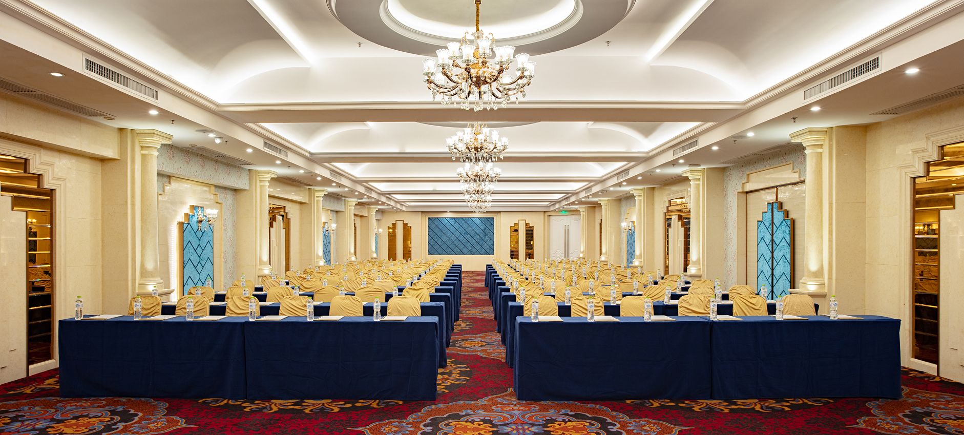 A conference room with rows of tables, a chandelier, and a patterned carpet.