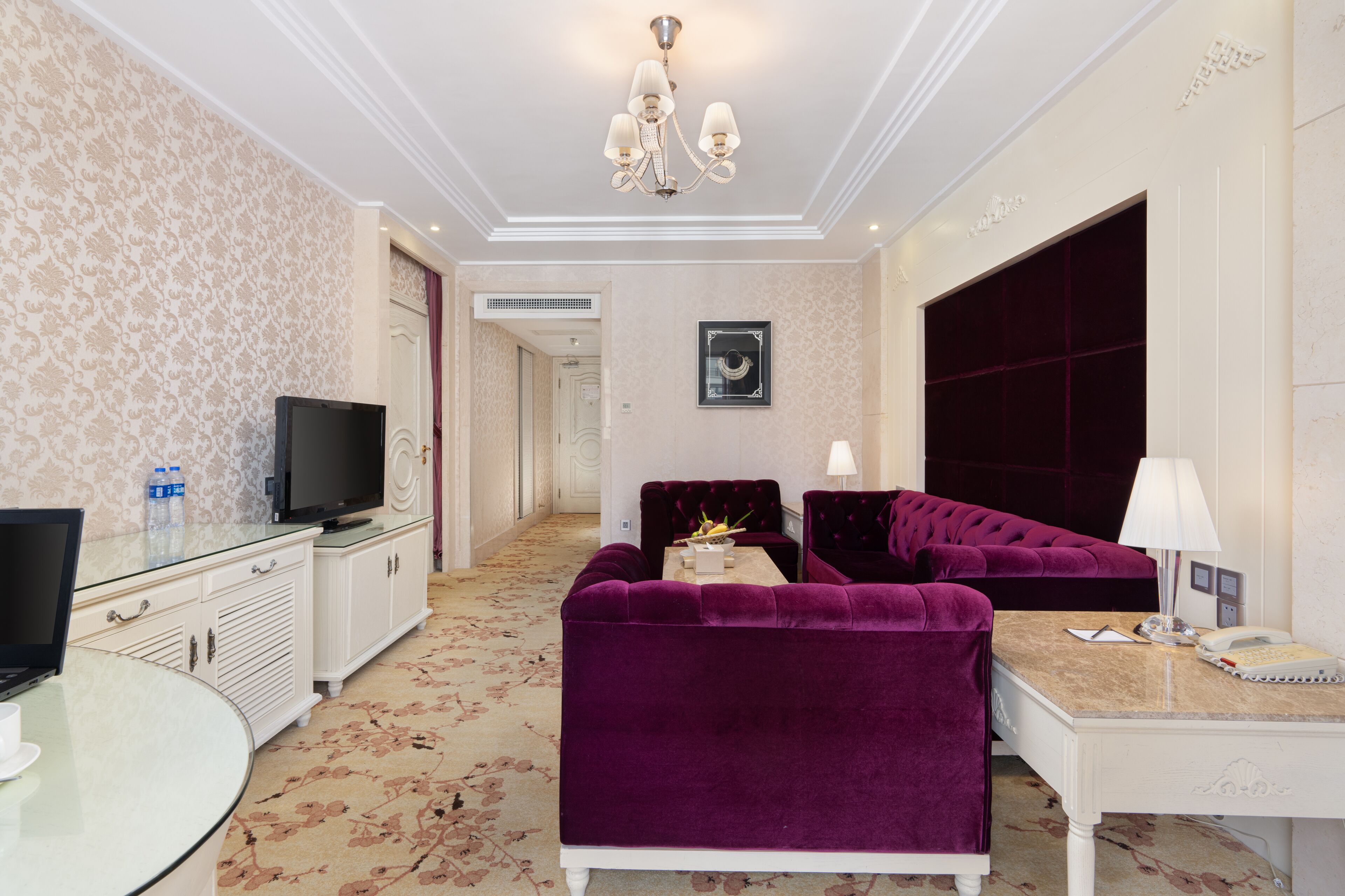 A hotel room with a TV, a sofa, a desk with a lamp, and a large wardrobe.