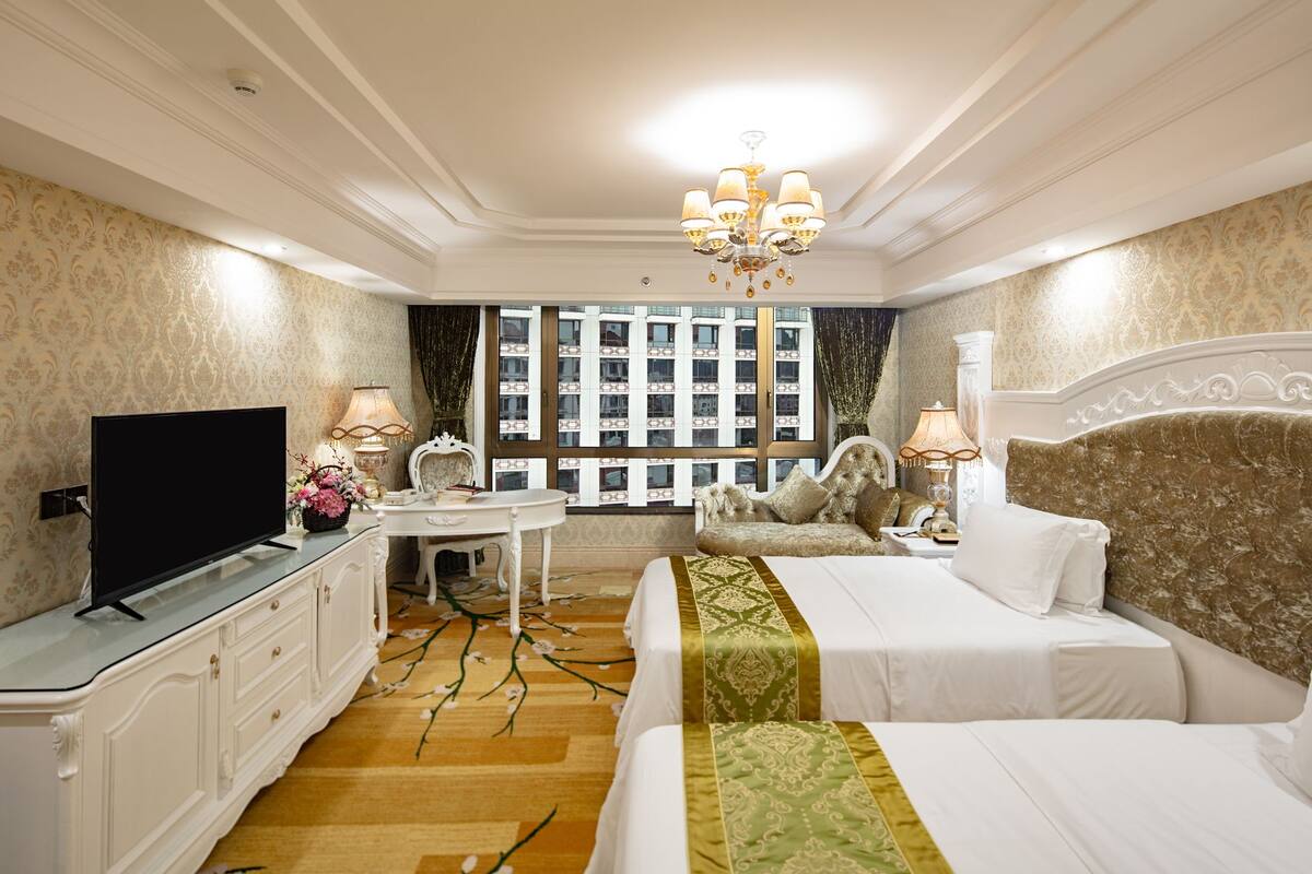 A hotel room with a bed, a desk, a television, and a window with a view of buildings.