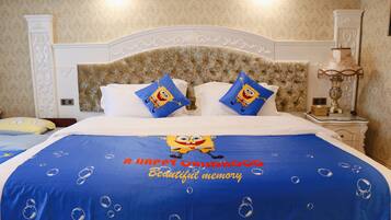 Una habitación de hotel con una cama que incluye una colcha azul con diseño de Bob Esponja y almohadas, un cabecero blanco y una mesita de noche con una lámpara.