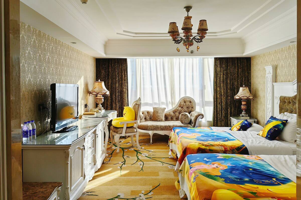 A hotel room with a bed, a chair, a desk, a television, and a chandelier.