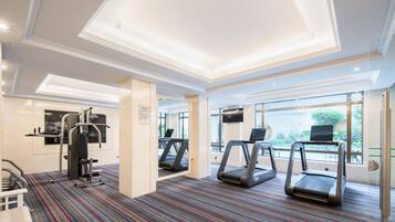 Ett hotells gym med löpband, en styrketräningsmaskin och ett stort fönster med utsikt över omgivningarna.