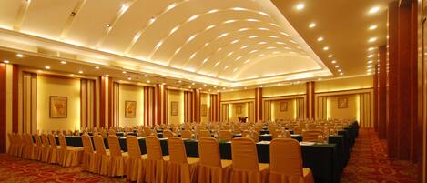 A conference room with rows of tables and chairs, a patterned carpet, and a high ceiling with recessed lighting.