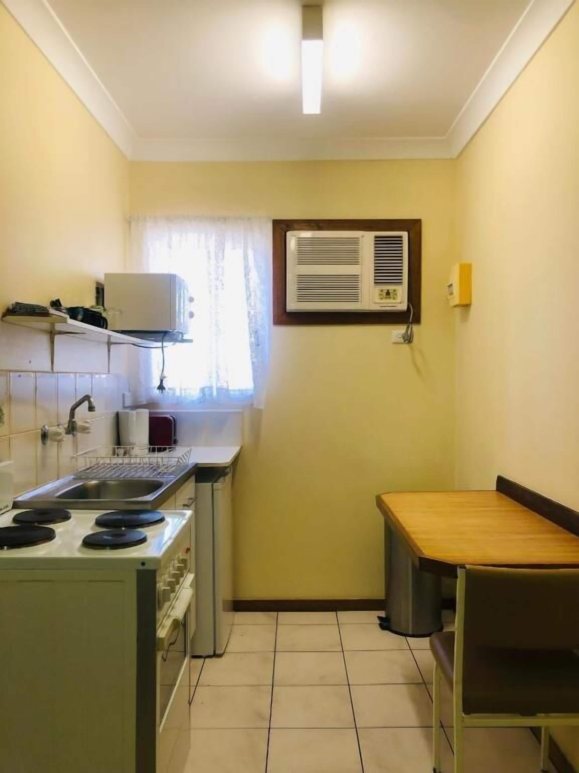 Cocina compacta con estufa, lavamanos y una pequeña mesa de comedor.