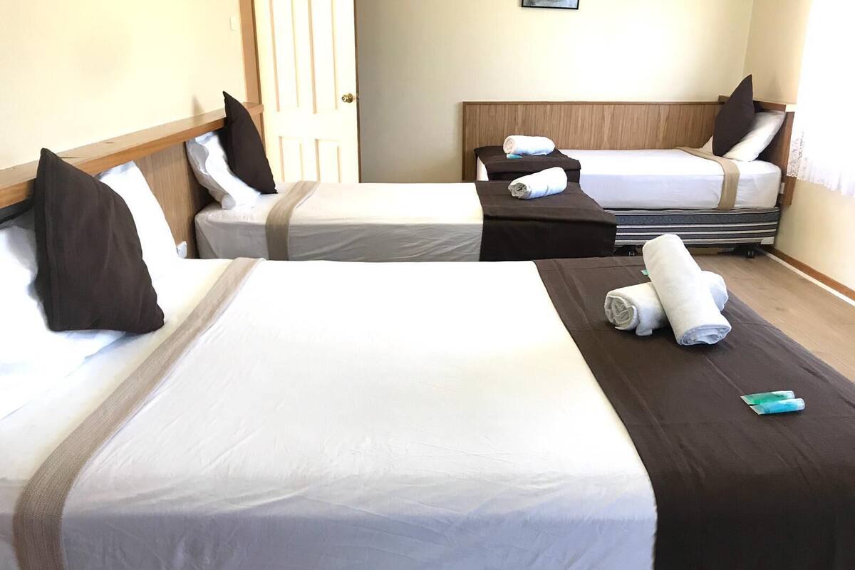 A hotel room with two beds, each with white linens and brown headboards. There are towels and a pair of slippers on the beds.