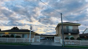 A motel with a gated driveway, a parking area, and a clear sky. - Angel's Rest Motel (Moree)