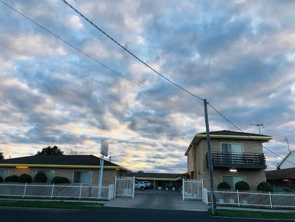 A motel with a gated driveway, a parking area, and a clear sky.