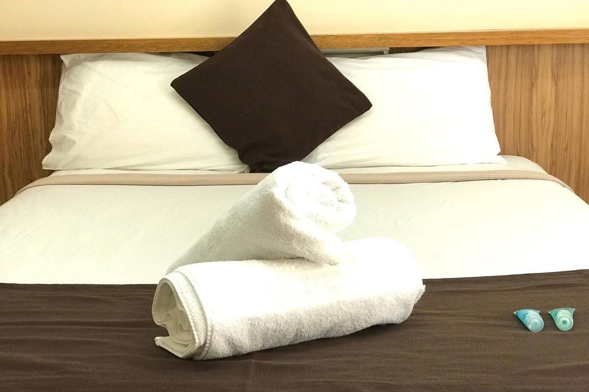 A neatly made bed with white and brown bedding, a folded white towel, and two small blue items on the bed.